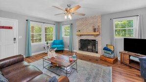 A living room with a fireplace, a blue sofa, a leather couch, and a television. - Bright & Cheery Bungalow - Mins to Downtwn Fort Mill (Fort Mill)