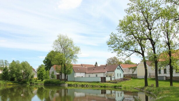 Un paisible village au bord d’un lac, avec ses maisons traditionnelles, un étang tranquille et une végétation luxuriante.