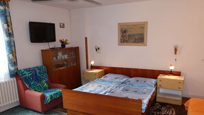 Une chambre à coucher avec un lit, une chaise, une commode, un téléviseur et un tableau accroché au mur.