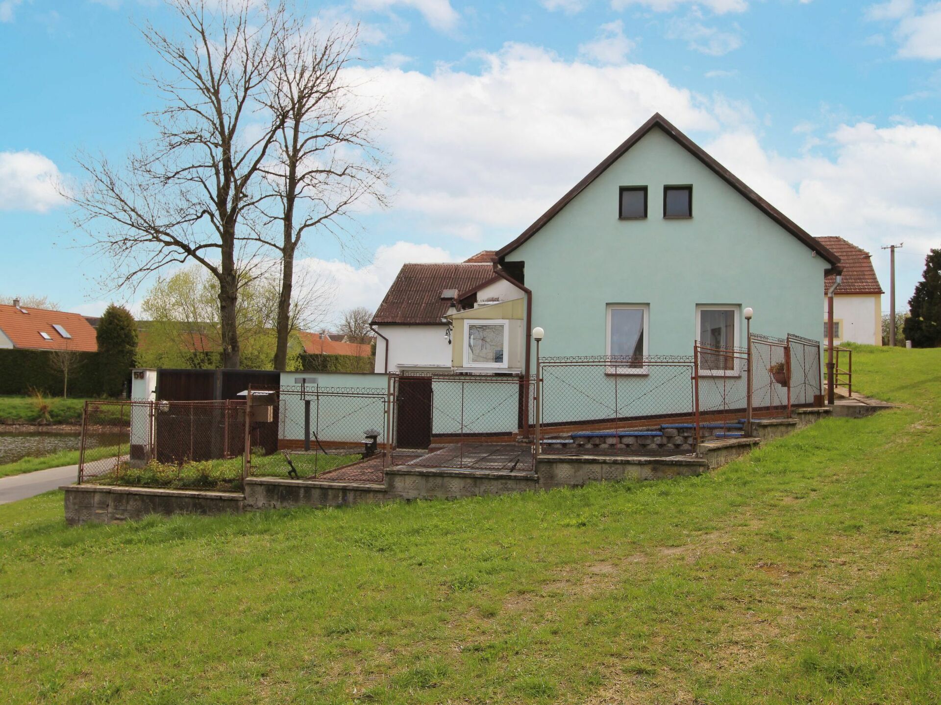 A light green house with a sloped roof, two windows, and a fenced yard.