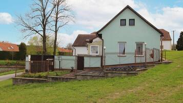 A light green house with a sloped roof, two windows, and a fenced yard.