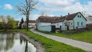 Un étroit sentier mène à une rangée de maisons bleu clair, avec un étang d’un côté.