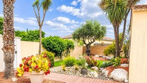 Um jardim com diversas plantas, um deck de madeira e um caminho pavimentado.