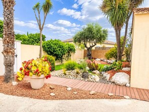 A garden with a variety of plants, a wooden deck, and a paved walkway. - Beautiful private villa for 6 guests with WIFI, private pool, A/C, TV and terrace (Thézan-lès-béziers)