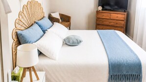 Ein ordentlich eingerichtetes Schlafzimmer mit einem Bett, Nachttischlampen, einem Fernseher und einem Wandbild.