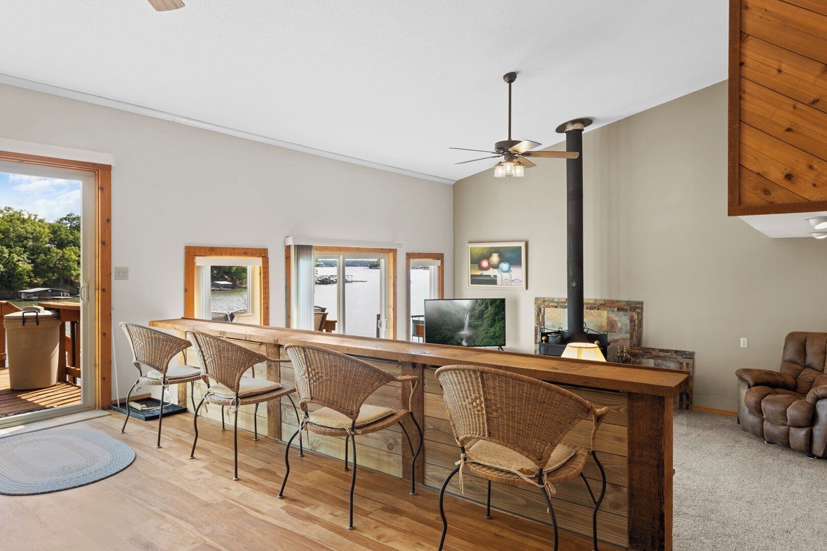 Une cuisine moderne avec un îlot central en bois, des chaises en osier, un téléviseur et une cheminée.