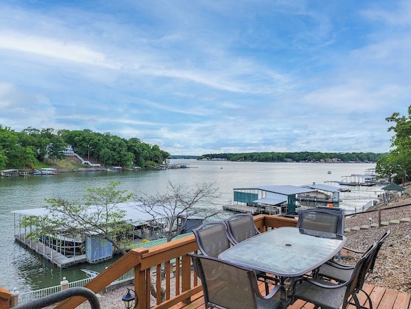 A lakeside deck with a table and chairs, docked boats, and a house with a staircase.
