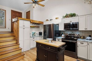 A kitchen with wooden stairs, a central island, stainless steel appliances, and white cabinetry.