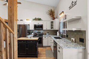 Cozinha moderna com armários brancos, bancada de granito, eletrodomésticos de aço inoxidável e uma placa decorativa na parede.