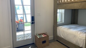 Een slaapkamer met een stapelbed, een deur met uitzicht naar buiten, en een rieten mand met een etiket.