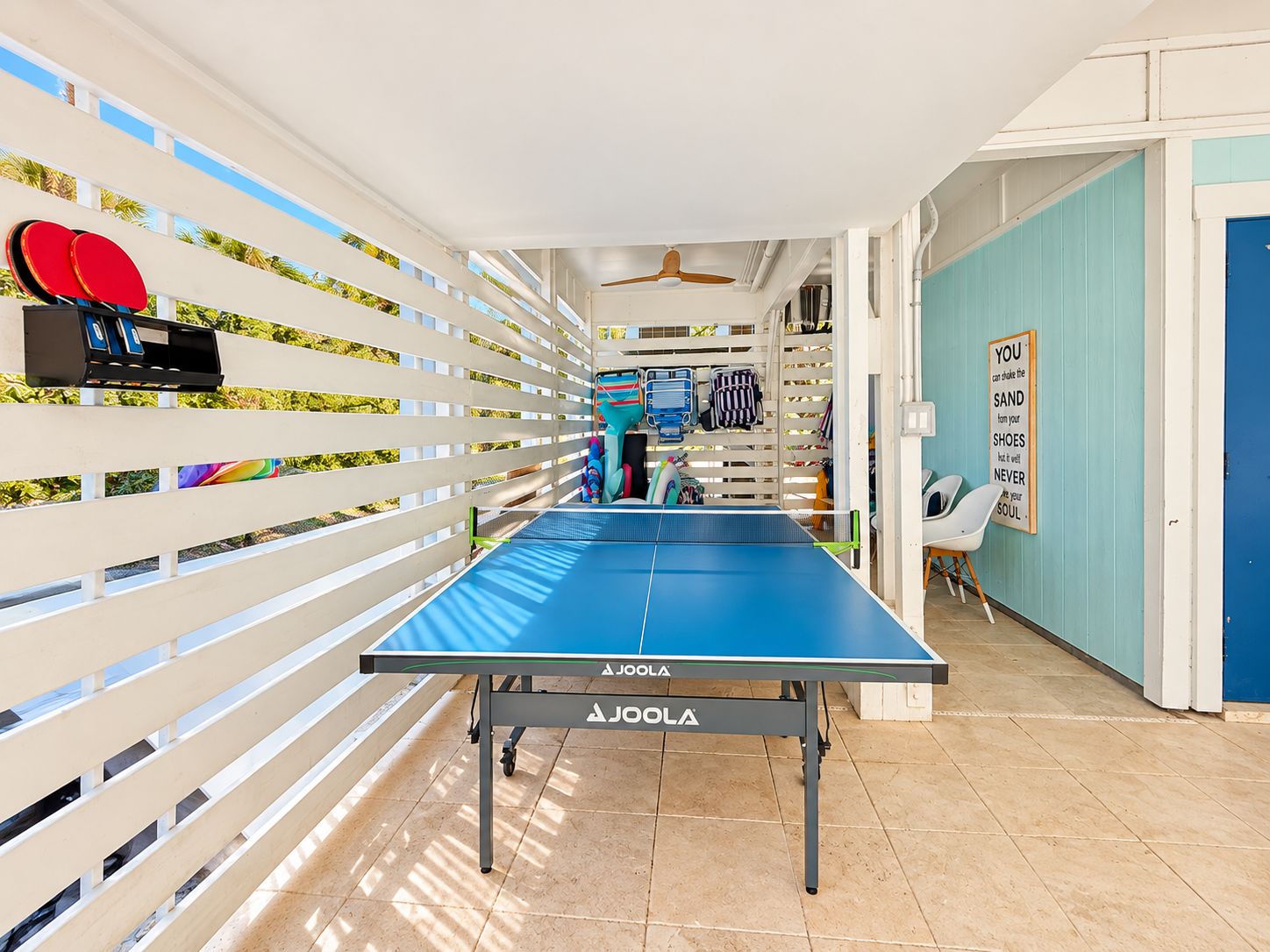 A ping pong table with a blue surface, white slatted walls, and a blue door.