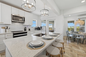 A modern kitchen with white cabinetry, stainless steel appliances, a central island with seating, and pendant lighting.