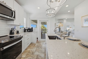 A modern kitchen with white cabinetry, a stainless steel range, and a large island with a sink.
