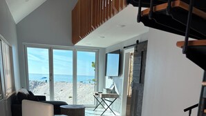 Ett rymligt vardagsrum med ett stort fönster med utsikt över en strand, en vit soffa och ett marmorgolv.
