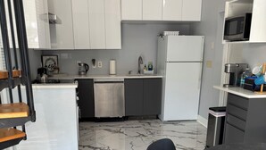 Ett modernt kök med vita skåp, diskmaskin, kylskåp och mikrovågsugn.