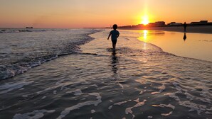 Una playa con una persona caminando por la orilla al atardecer.