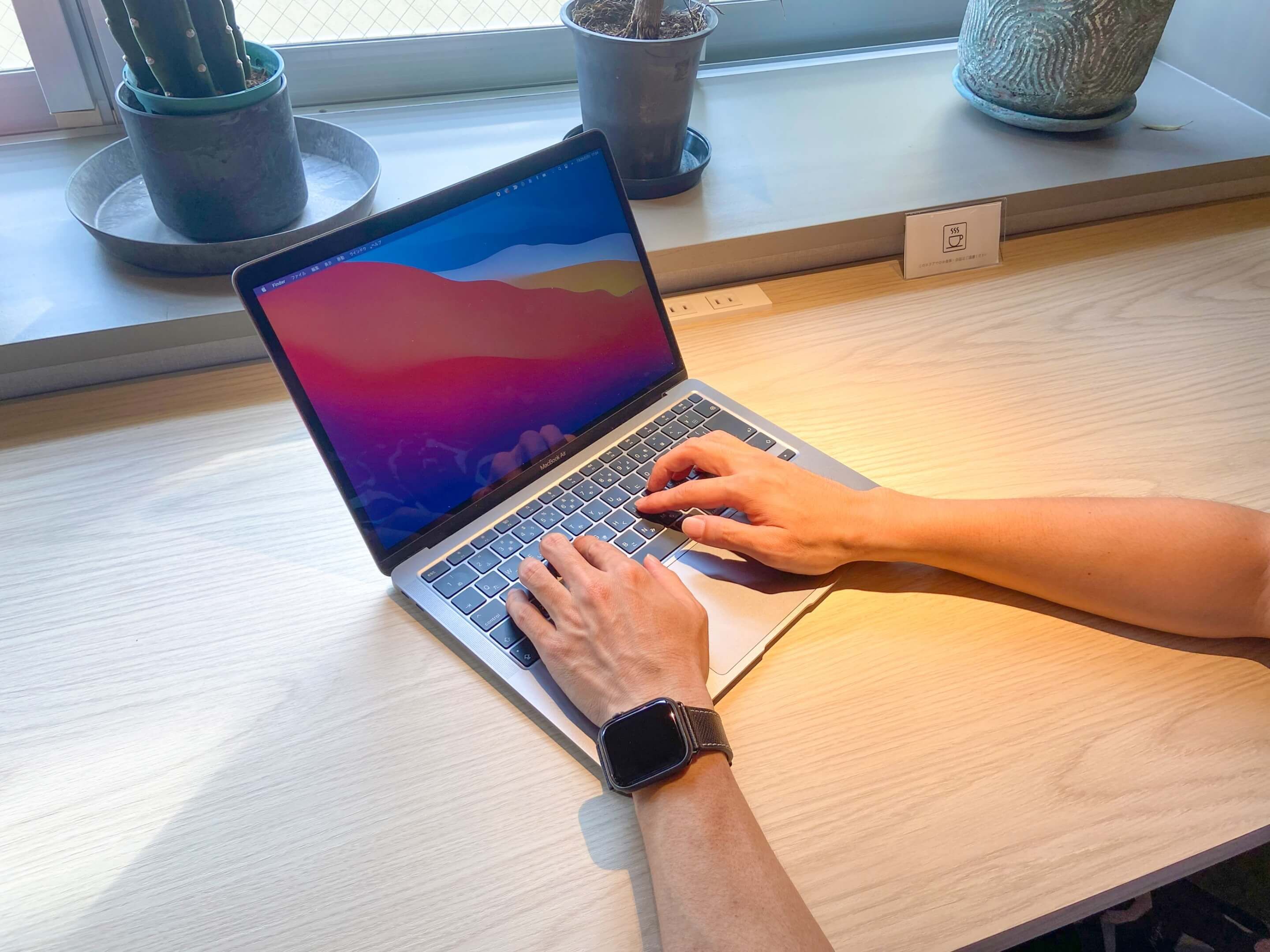 Een laptop op een houten tafel, met een raam op de achtergrond.