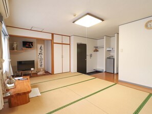 A traditional Japanese-style room with tatami flooring, a television, a desk with a lamp, and a sliding door leading to a bathroom. - Deigo Hotel (Okinawa)