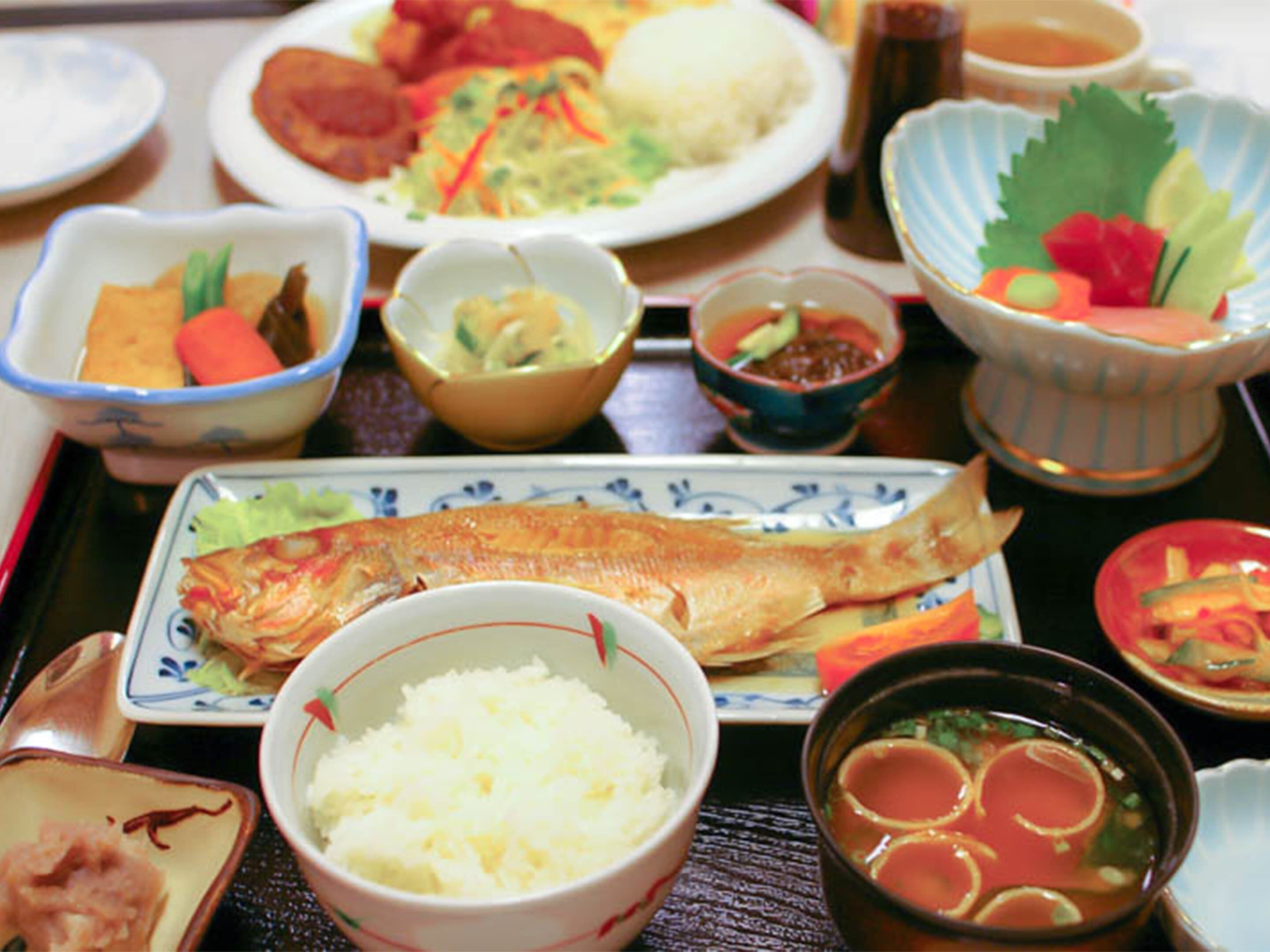A variety of dishes including fish, rice, and vegetables, served on a tray.