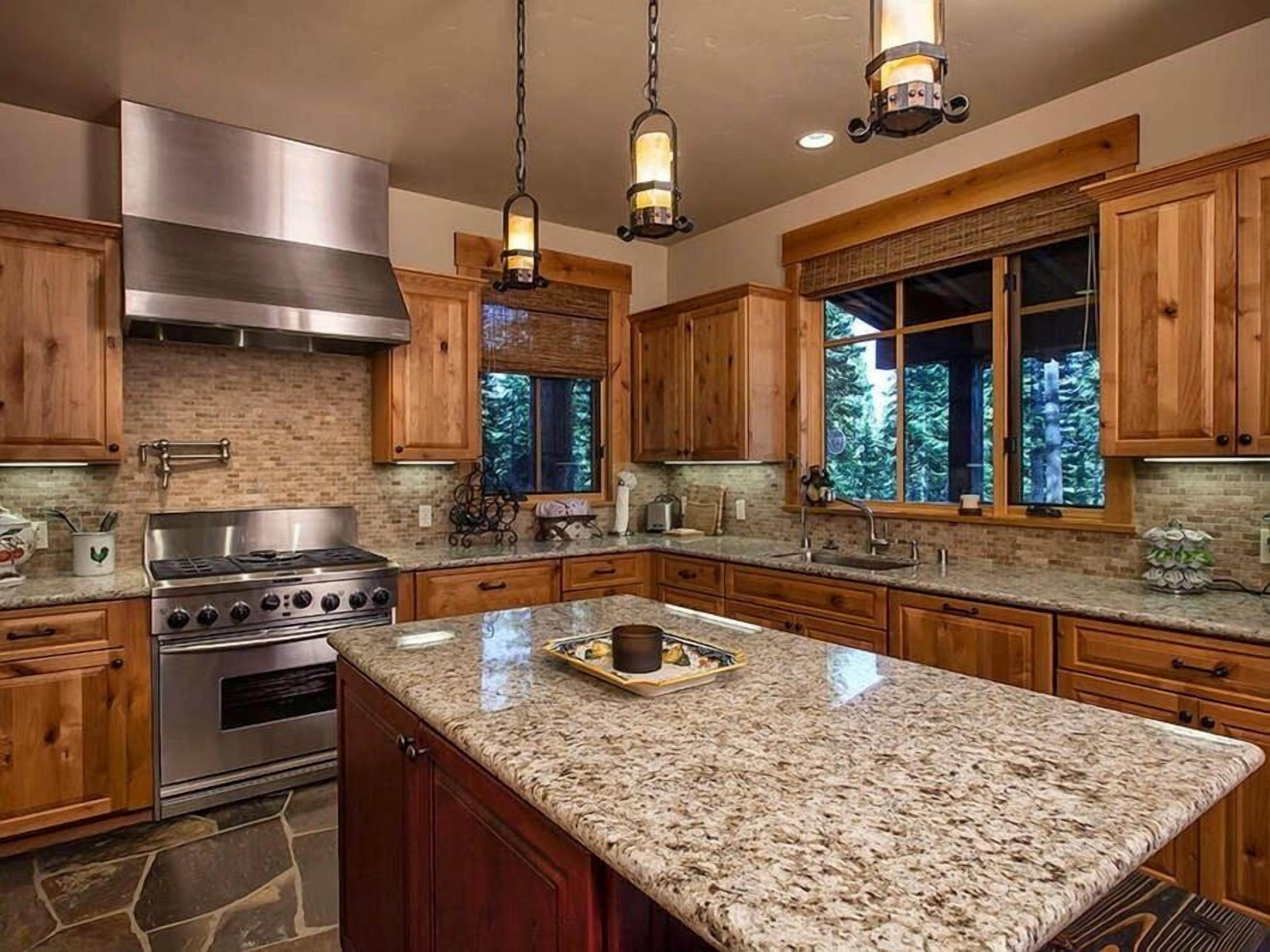 A kitchen with granite countertops, wooden cabinets, a stainless steel stove, and pendant lighting.
