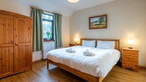 Un dormitorio con cama de madera, dos mesitas de noche con lámparas, una ventana con cortinas, un radiador y un armario de madera.
