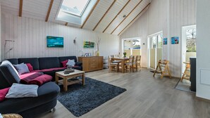 A spacious living area with a high ceiling, wooden beams, a large window, a sofa, a dining table, and chairs.