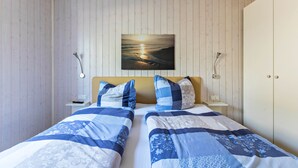 A bedroom with two beds, a wooden ceiling, a wall-mounted painting, bedside lamps, and a wardrobe.