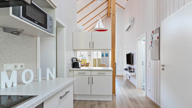 A modern kitchen with white cabinetry, a built-in microwave, and a wooden ceiling.