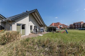 Une maison d’habitation avec un toit en pente, une terrasse dotée de mobilier d’extérieur et une cour gazonnée.