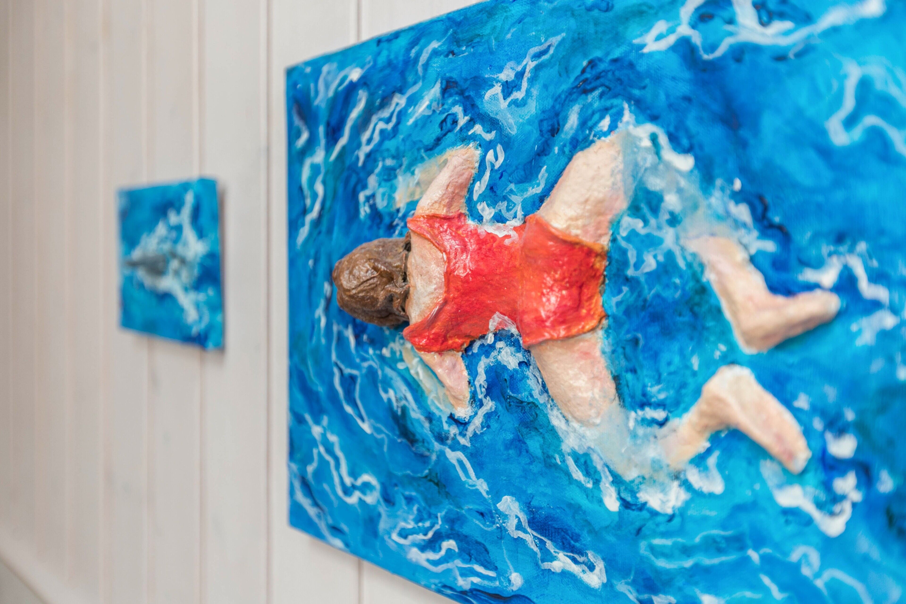 Una pintura de una persona en traje de baño rojo nadando en agua azul.