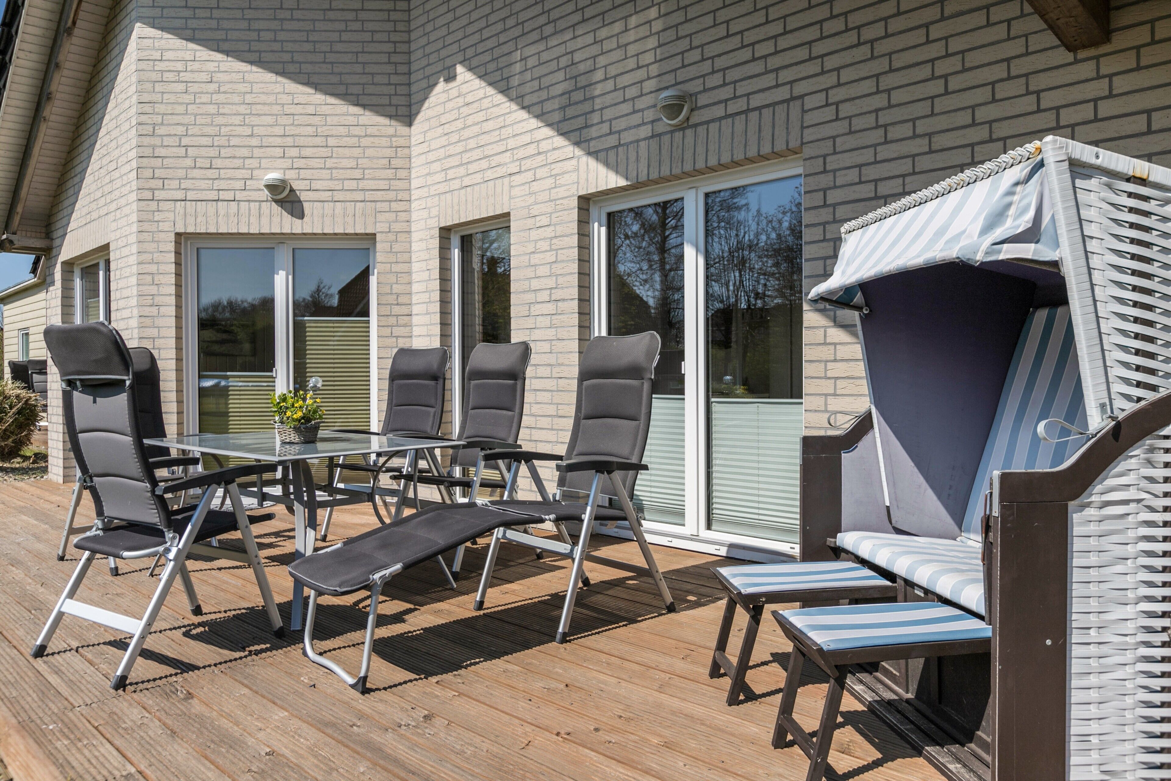 Une terrasse extérieure avec une table et des chaises, un espace salon couvert et un bâtiment en briques en arrière-plan.