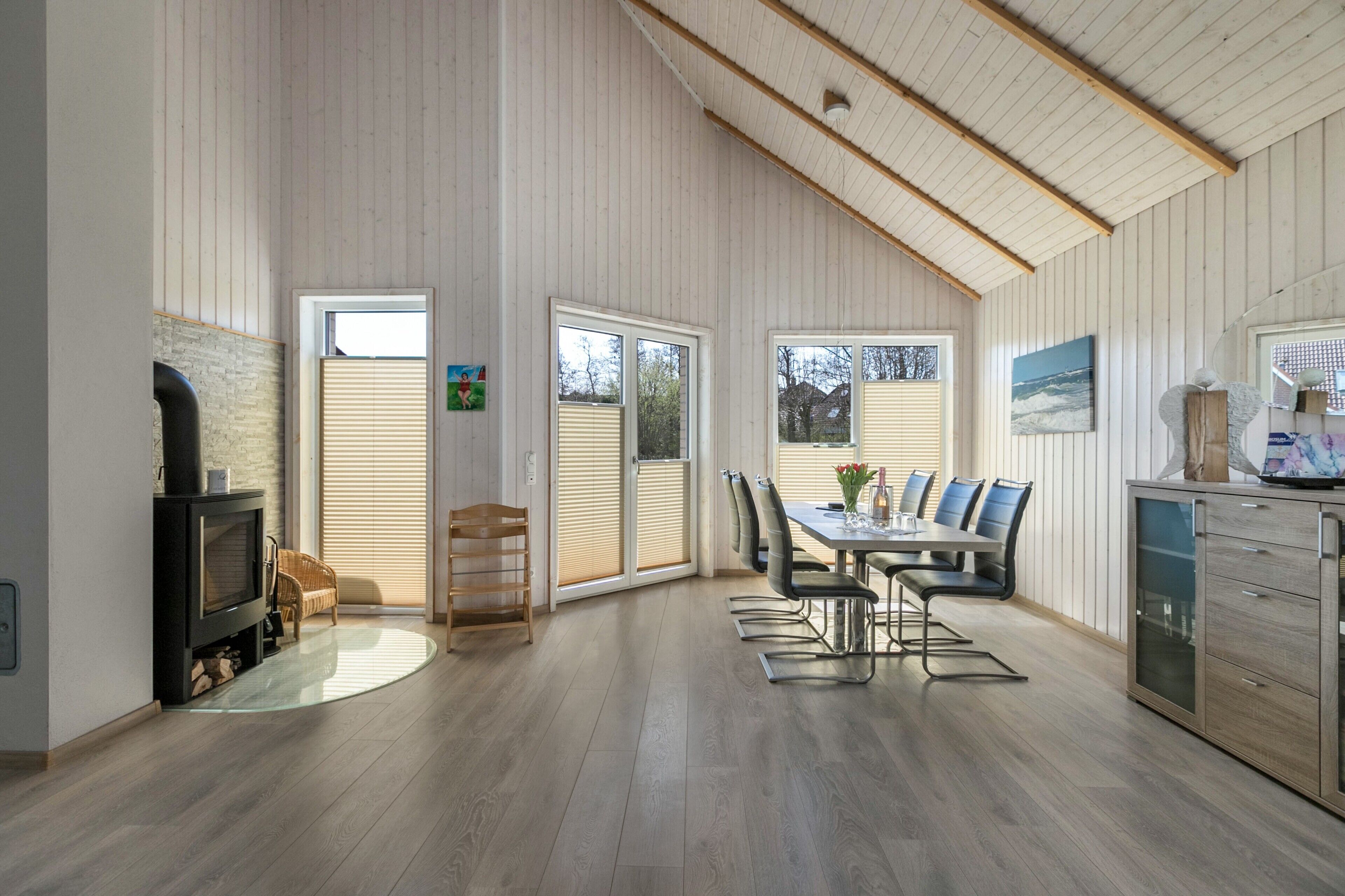 Una habitación amplia con chimenea, una mesa de comedor con sillas, zona de cocina y ventanas grandes.