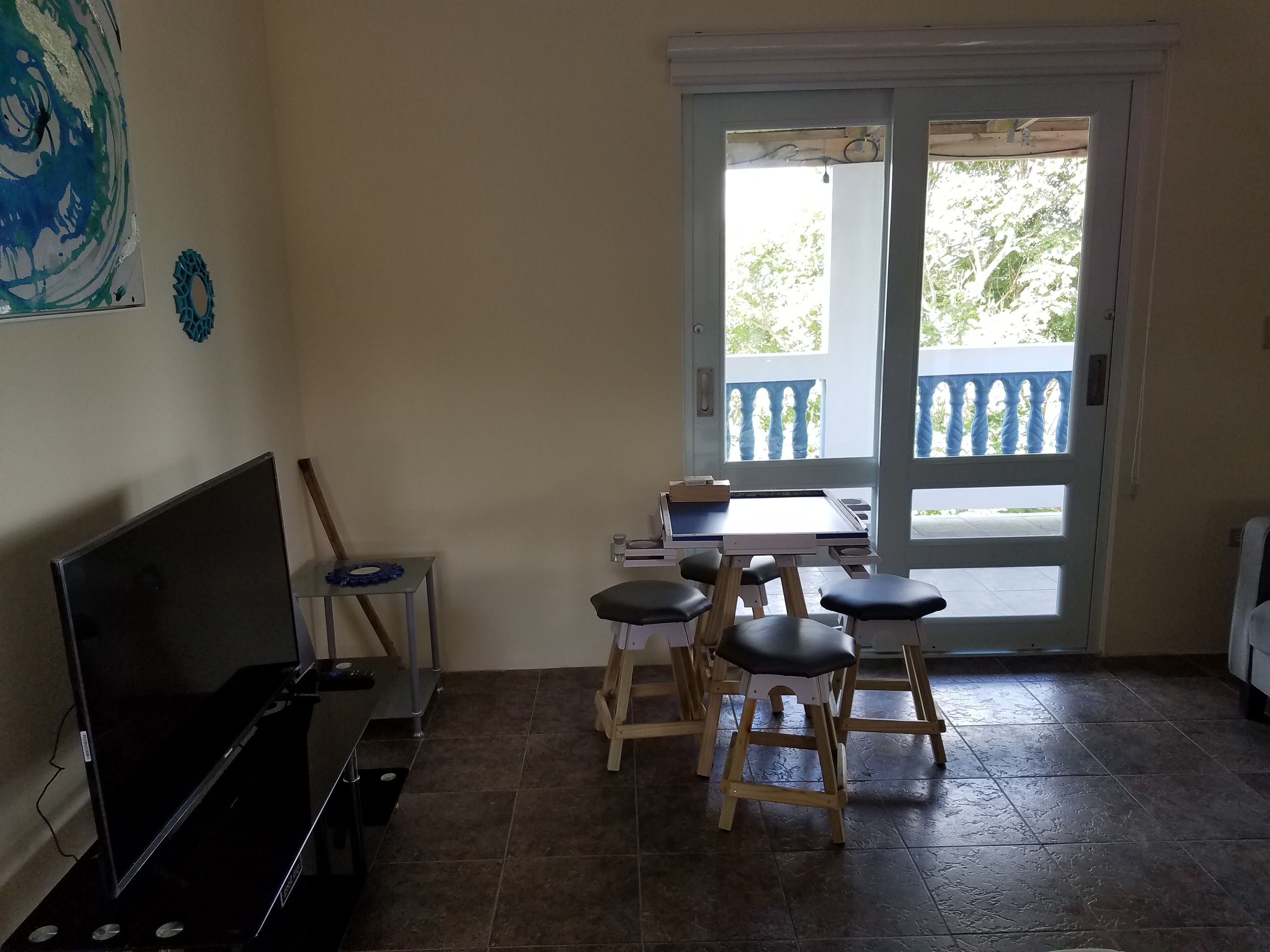 Habitación con televisión, una pequeña mesa con sillas, ventana con vista a árboles y puerta que da al exterior.