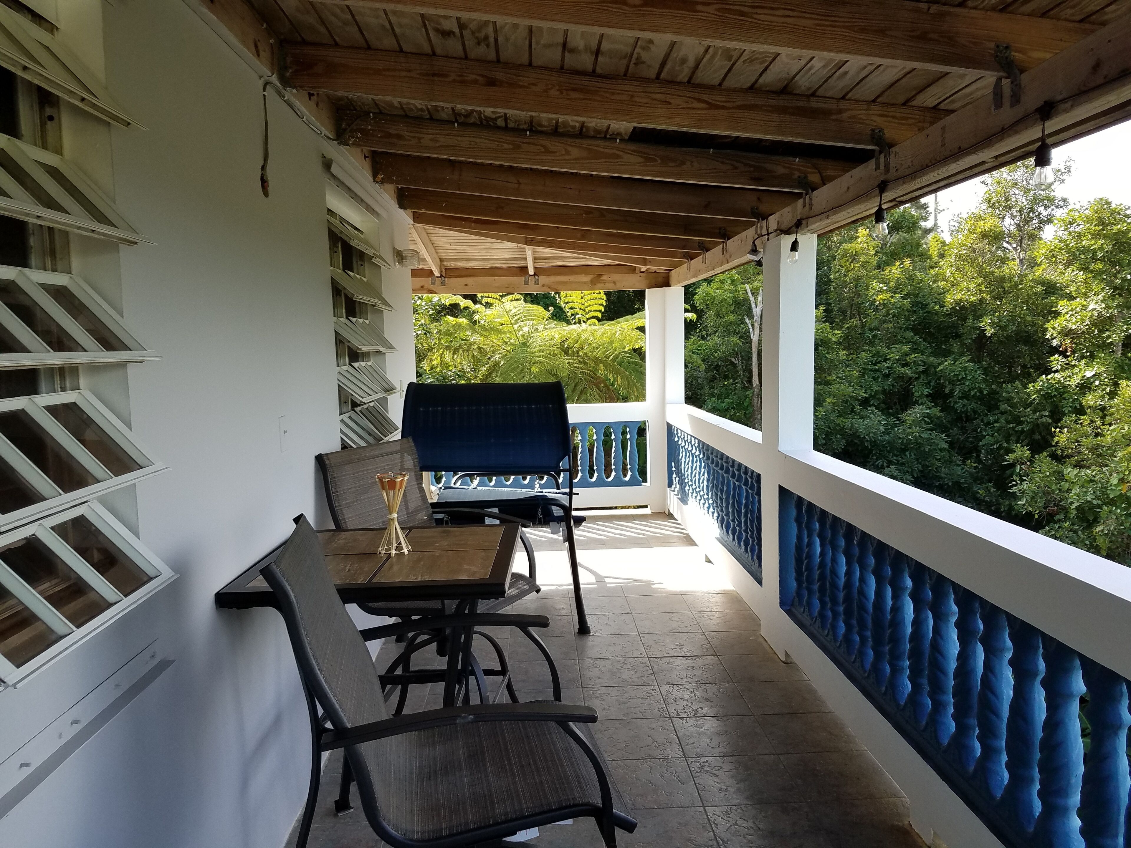 En inglasad balkong med ett bord och stolar, utsikt över grönområden och ett vitt räcke.