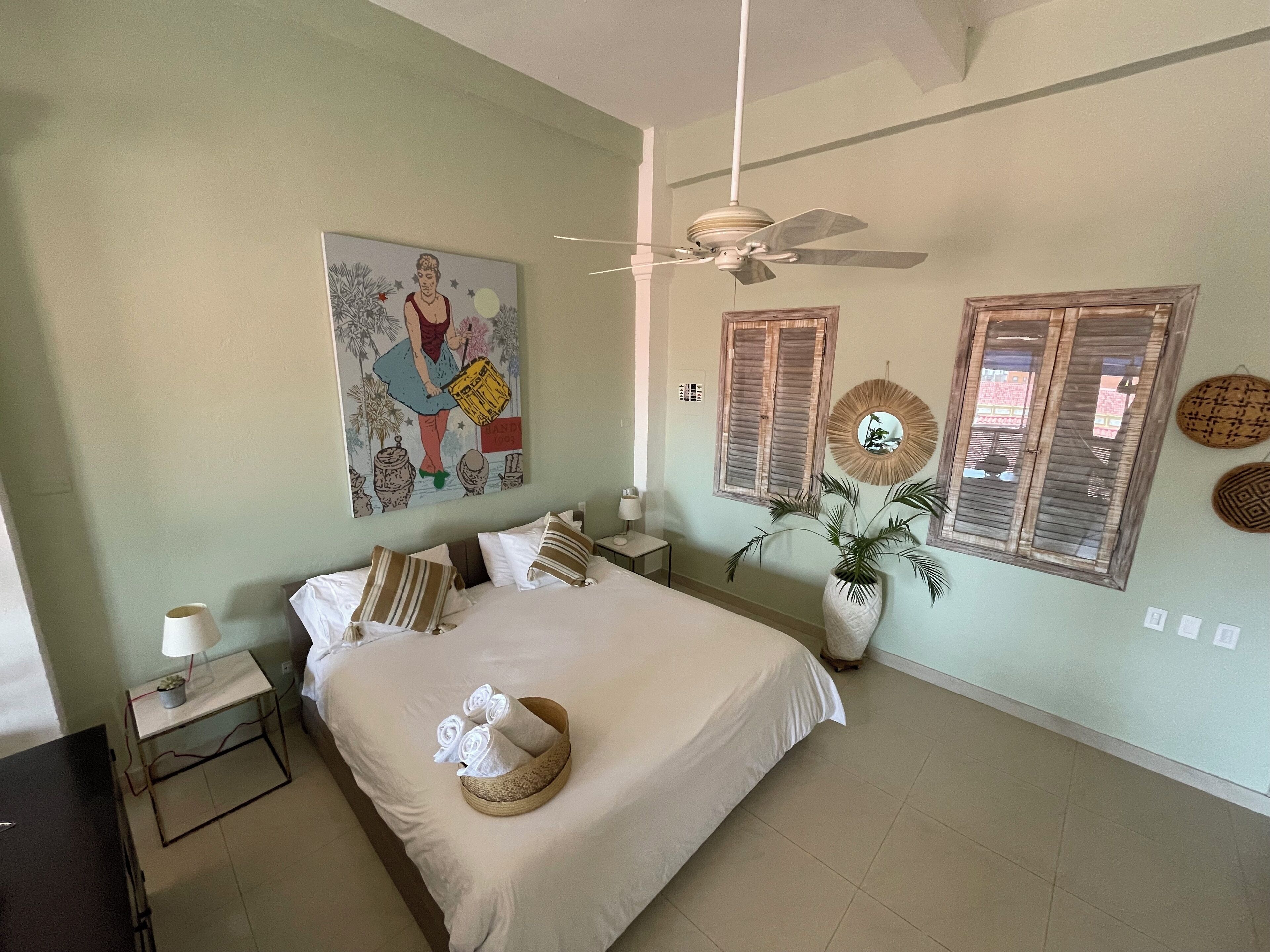 Une chambre à coucher avec un lit, un ventilateur de plafond, un tableau et une plante en pot.
