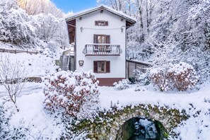 A two-story chalet with a balcony, surrounded by snow-covered trees and a stone bridge. - House By The Stream in Soča Valley, Kanal ob Soči, Slovenia (Kanal ob Soči)