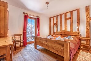 A wooden bed with a headboard, a wooden desk, and a chair in a room with a view of a snowy landscape through a window. - House By The Stream in Soča Valley, Kanal ob Soči, Slovenia (Kanal ob Soči)