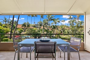 A balcony with a table and chairs, overlooking a tropical landscape with palm trees and a pool.