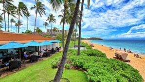 A beachside resort with outdoor seating, palm trees, and a view of the ocean. - Aston Maui Kaanapali Villas 262 | Tropical Garden Views – Pool, Hot Tub & Spa (Lahaina)