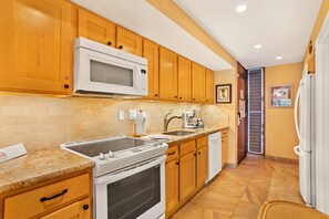 A kitchen with wooden cabinets, a microwave, a stove, a sink, and a refrigerator. - Aston Maui Kaanapali Villas 262 | Tropical Garden Views – Pool, Hot Tub & Spa (Lahaina)