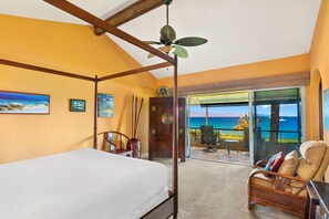 Quarto com cama de dossel, ventilador de teto e vista para o oceano através de uma porta de vidro deslizante.