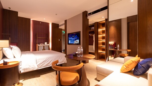 A hotel room with a bed, a sofa, a chair, a TV, and a small table with a lamp. - Foshan Xinxuangong Hotel  (Foshan)