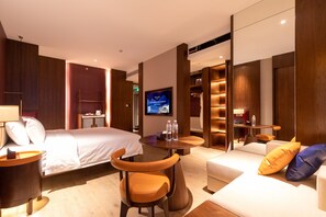 A hotel room with a bed, a sofa, a chair, a TV, and a small table with a lamp. - Foshan Xinxuangong Hotel  (Foshan)