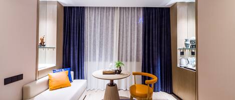 A modern hotel room with a sofa, a small round table, a chair, a window, and a curtain.