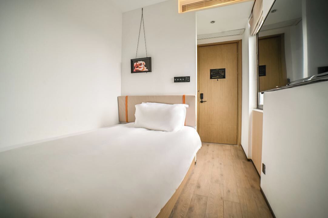 Quarto de hotel com cama, porta de madeira e um pequeno corredor.
