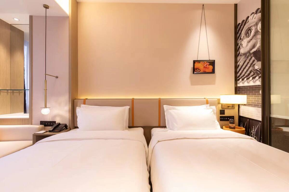 Habitación de hotel con dos camas, una mesita de noche con teléfono, una lámpara y una obra de arte en la pared.
