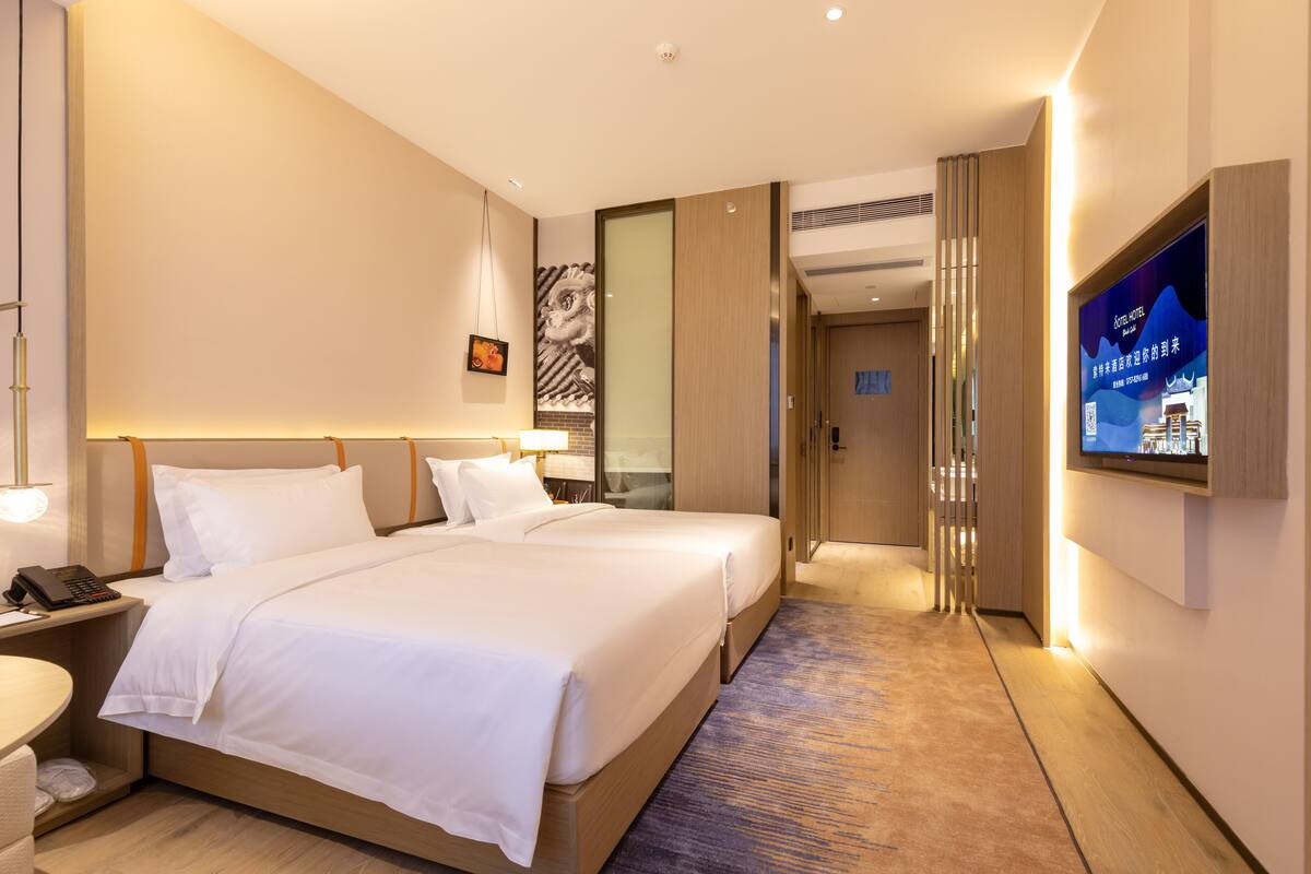 Una habitación de hotel con una cama grande, mesitas de noche, un televisor y piso alfombrado.