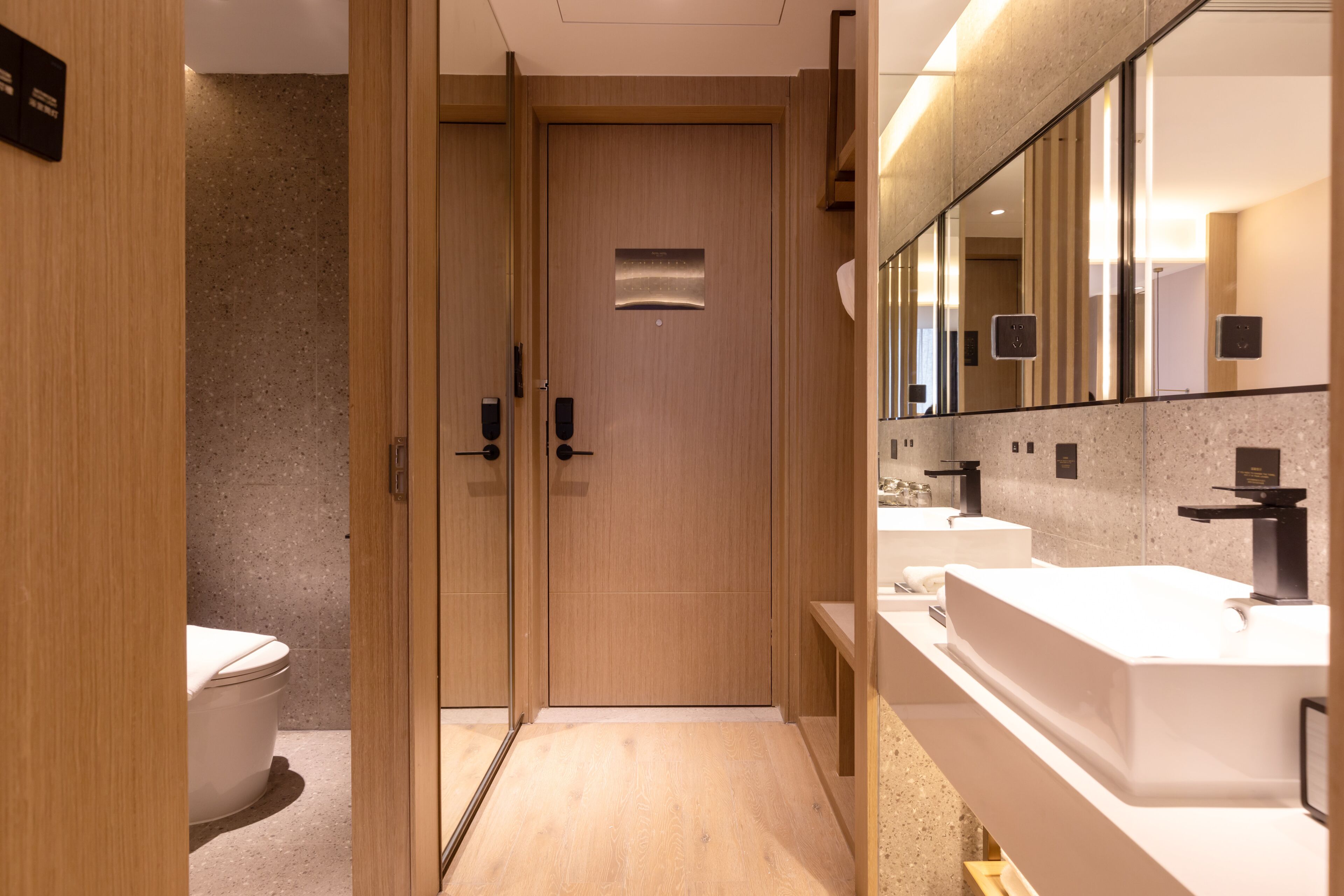 Ein modernes Badezimmer mit Holztüren, einer Toilette und zwei Waschbecken mit Spiegeln.