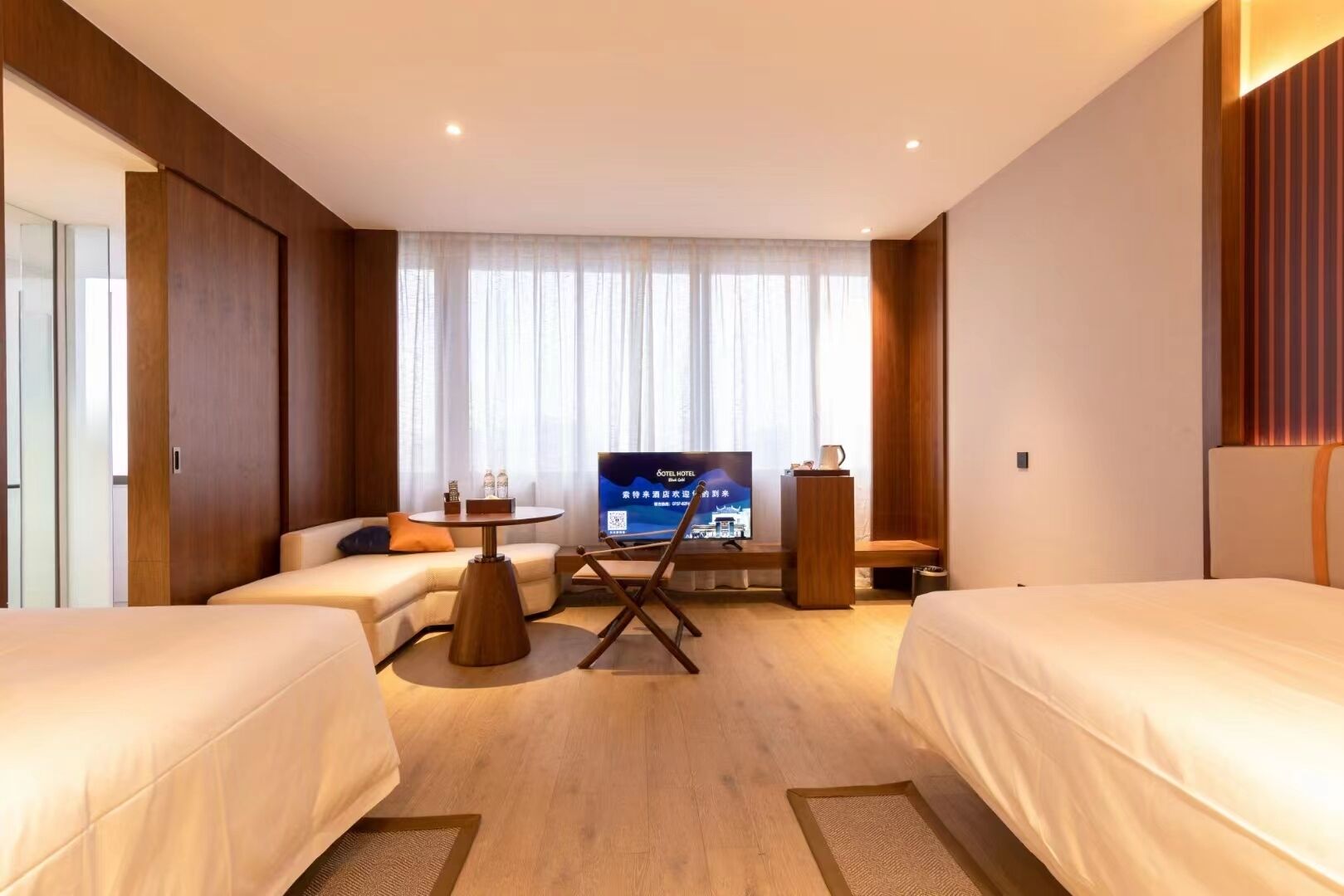 Une chambre d’hôtel avec deux lits, une télévision, une petite table avec une chaise et une fenêtre avec des rideaux.