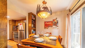 A dining area with a wooden table set for four, a chandelier, and a kitchen in the background. - Walk to Ski, Near Canyon Lodge, Quiet Getaway 512 (Mammoth Lakes)